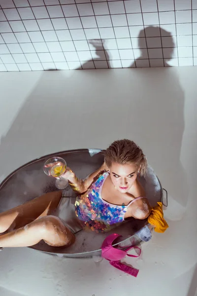 Belle jeune femme tenant verre à cocktail dans la baignoire de lavage dans la salle de bain avec espace de copie — Photo de stock