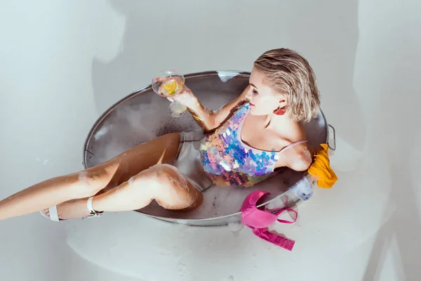 Vista superior de la hermosa mujer joven sosteniendo copa de cóctel en la bañera de lavado en el baño - foto de stock