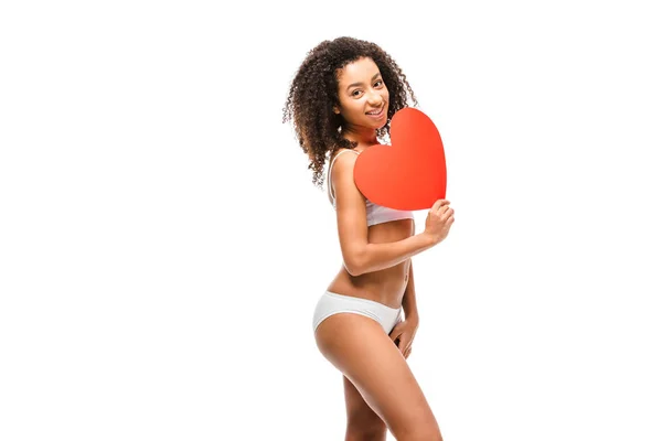 Hermosa sonriente afroamericana chica en ropa interior celebración de tarjeta en forma de corazón aislado en blanco - foto de stock