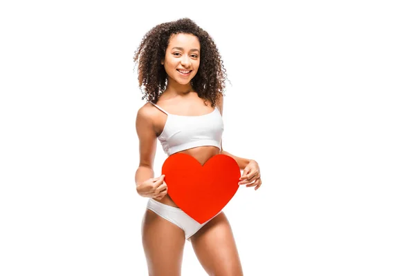 Afroamericana chica en ropa interior celebración de tarjeta en forma de corazón y mirando a la cámara aislada en blanco - foto de stock