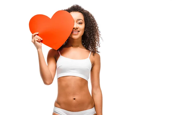 Hermosa chica afroamericana en ropa interior posando y sosteniendo tarjeta en forma de corazón aislado en blanco - foto de stock