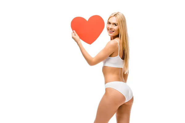 Beautiful smiling girl in underwear holding heart shaped card isolated on white — Stock Photo