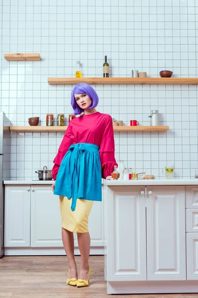 Belle femme au foyer avec des cheveux violets et des vêtements colorés posant dans la cuisine — Photo de stock