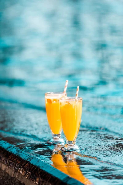 Orange cocktails with straws standing near swimming pool — Stock Photo