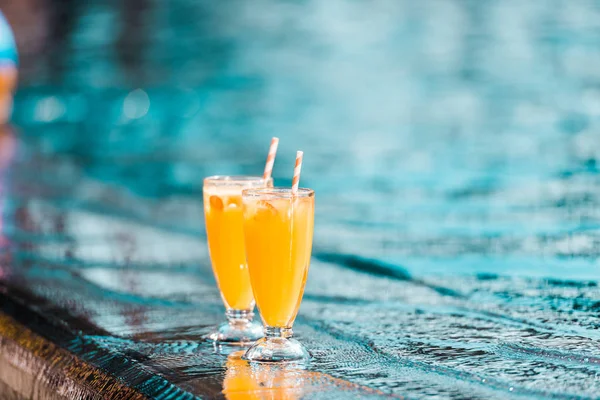 Deux verres à cocktails orange avec des pailles debout au bord de la piscine — Photo de stock