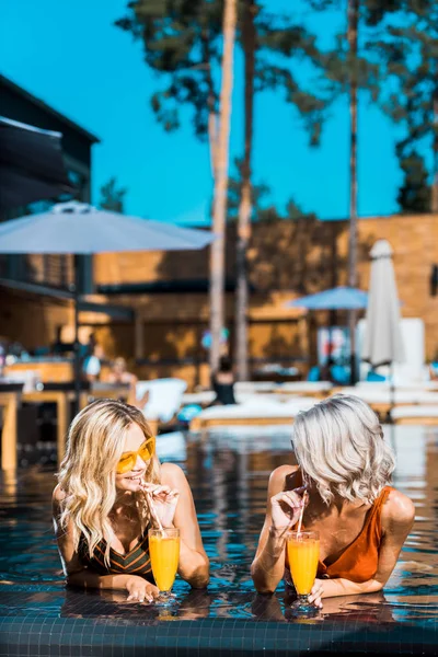 Mujeres elegantes que relajan en la piscina con cócteles - foto de stock