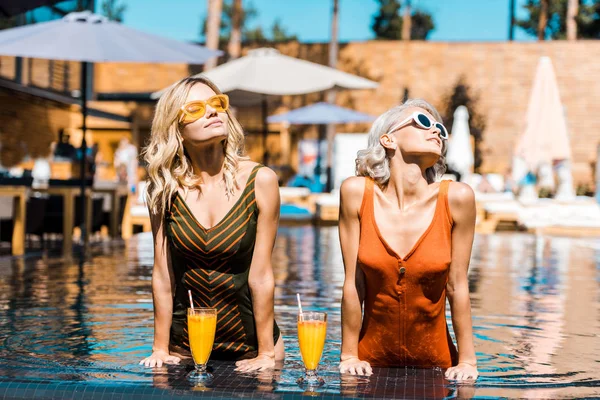 Mujeres elegantes y atractivas relajándose en la piscina con cócteles - foto de stock