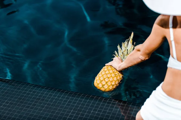 Partial view of girl posing with pineapple near swimming pool — Stock Photo