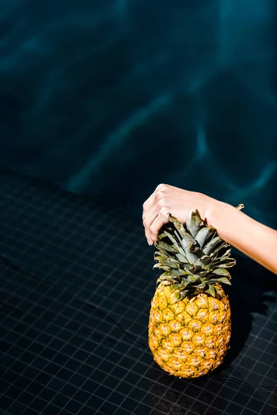 Partial view of woman posing with fresh pineapple near swimming pool — Stock Photo