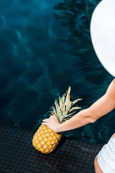 Visão parcial da mulher posando com abacaxi doce perto da piscina — Fotografia de Stock