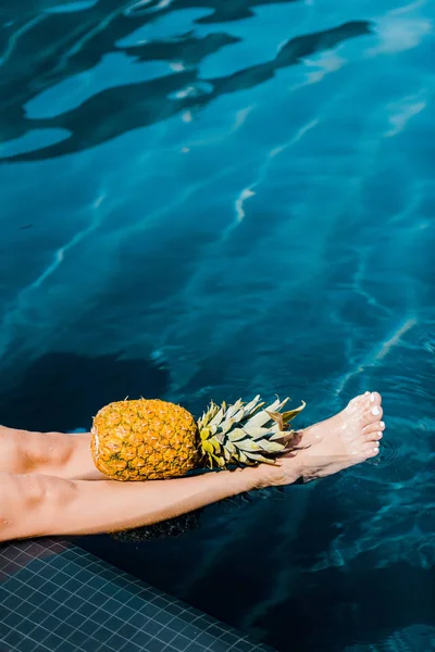 Visão de seção baixa da menina posando com abacaxi doce na beira da piscina — Fotografia de Stock