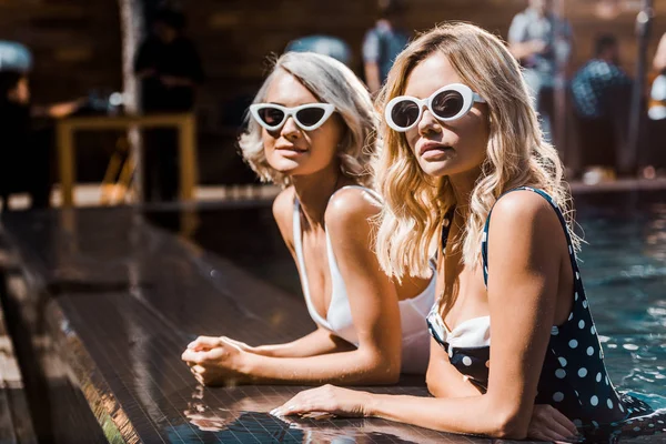 Meninas atraentes em óculos de sol posando na piscina — Fotografia de Stock