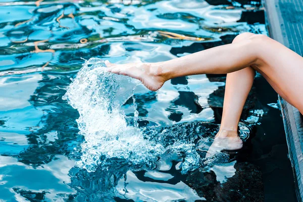 Vista recortada de la niña sentada cerca de la piscina con las piernas en el agua - foto de stock