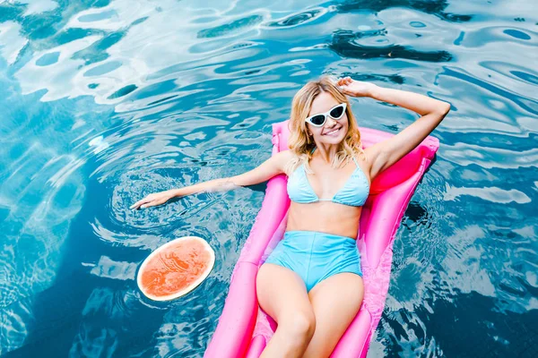 Atractiva chica sonriente en pin up traje de baño descansando en el colchón inflable rosa en la piscina - foto de stock