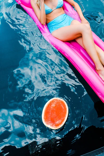 Cropped view of pin up girl lying on pink inflatable mattress in swimming pool with watermelon — Stock Photo