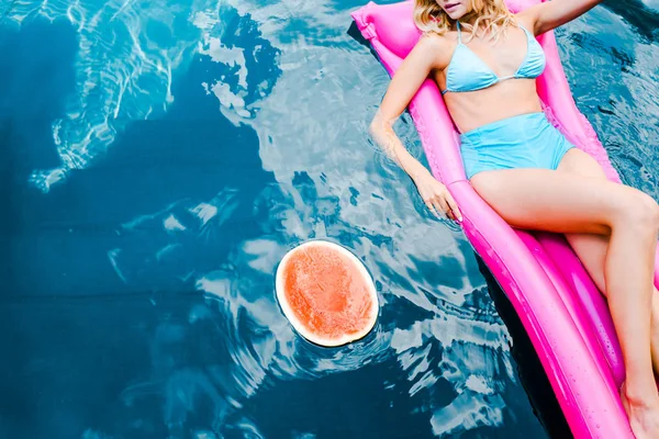 Cropped view of girl in swimsuit resting on pink inflatable mattress in swimming pool with watermelon — Stock Photo