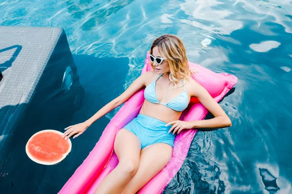 Beautiful girl in pin up swimsuit resting on pink inflatable mattress in swimming pool with watermelon — Stock Photo