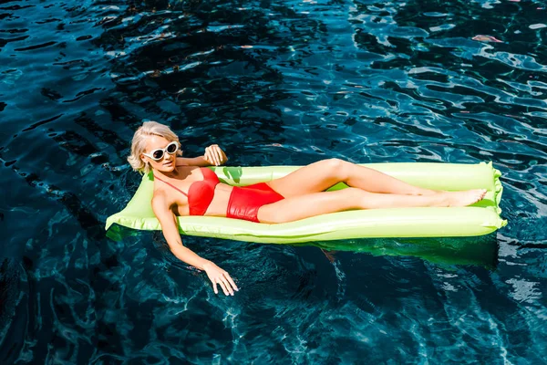 Красива молода жінка в купальнику розслабляється на зеленому надувному матраці в басейні — стокове фото