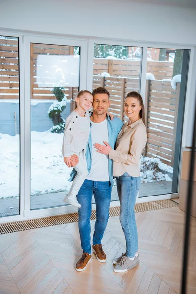Счастливый отец держит в руках веселую дочь, стоя рядом с женой в новом доме — стоковое фото