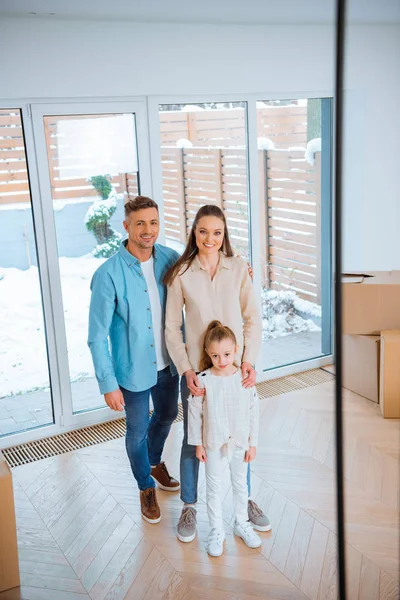 Happy husband and wife standing near cute daughter in new home — Stock Photo