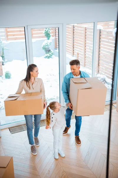 Bonito filha olhando alegre mãe e pai segurando caixas no novo lar — Fotografia de Stock