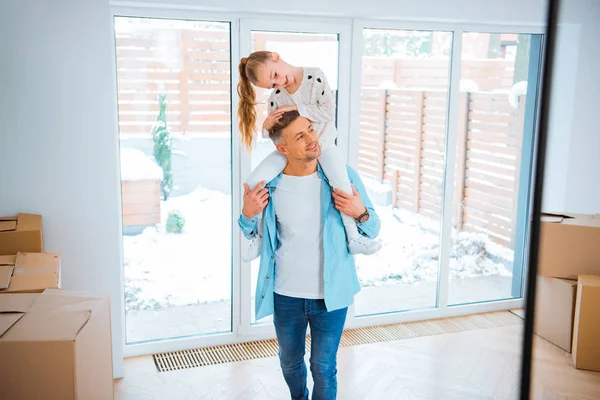 Bell'uomo che porta sul collo una figlia sorridente mentre cammina in una nuova casa — Foto stock