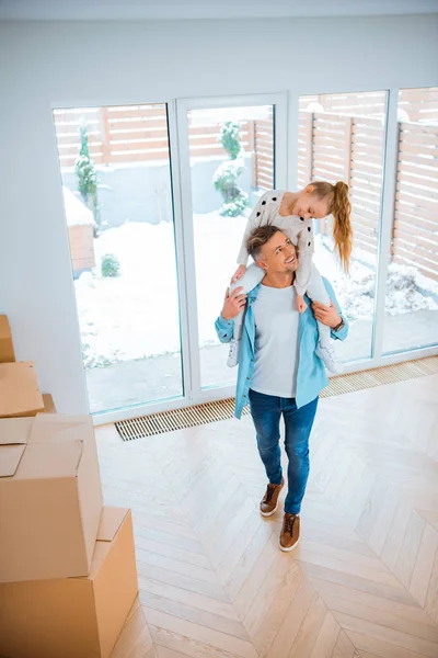 Smiling daughter looking at cheerful father carrying on neck while walking in new home — Stock Photo