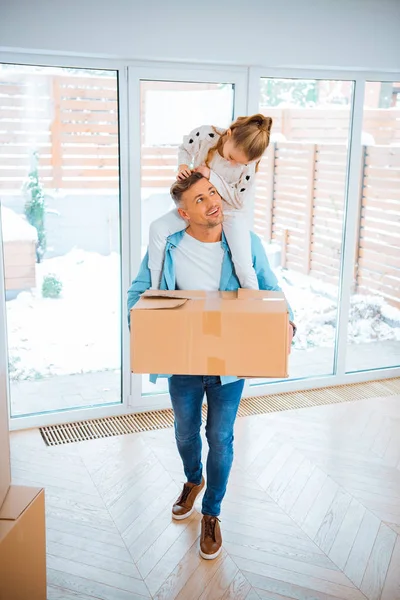 Happy father carrying on neck smiling daughter while holding box in new home — Stock Photo