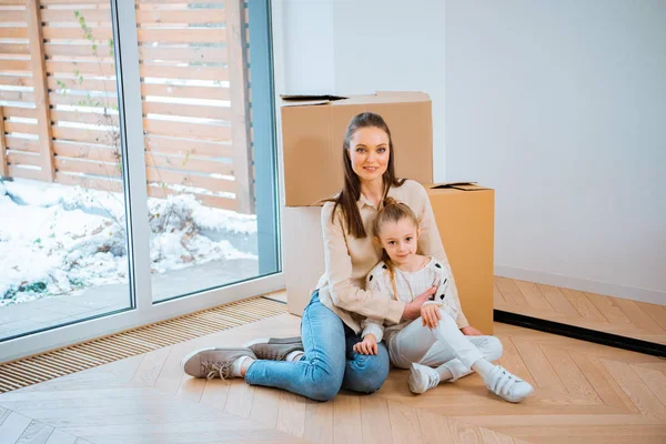 Весела мати обіймає милу дочку, сидячи на підлозі в новому будинку — стокове фото