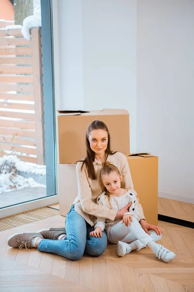 Belle mère embrassant fille tout en étant assis sur le sol dans une nouvelle maison — Photo de stock