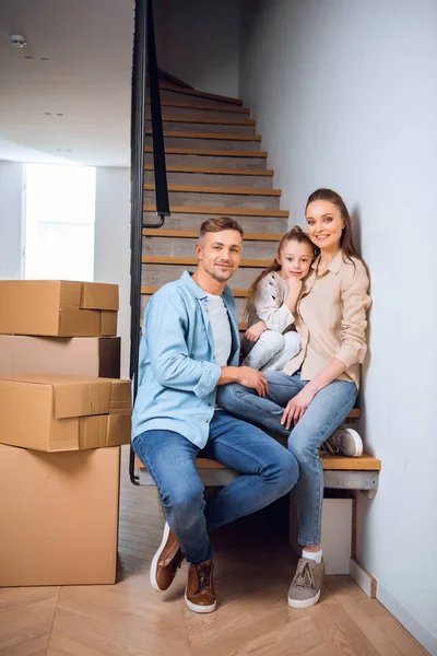 Glückliche Familie lächelt, während sie im neuen Zuhause auf der Treppe sitzt — Stockfoto