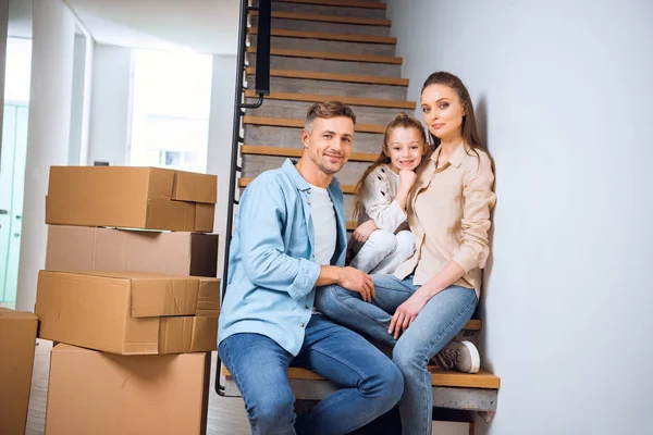 Alegre familia sonriendo mientras está sentado en escaleras en nuevo hogar - foto de stock