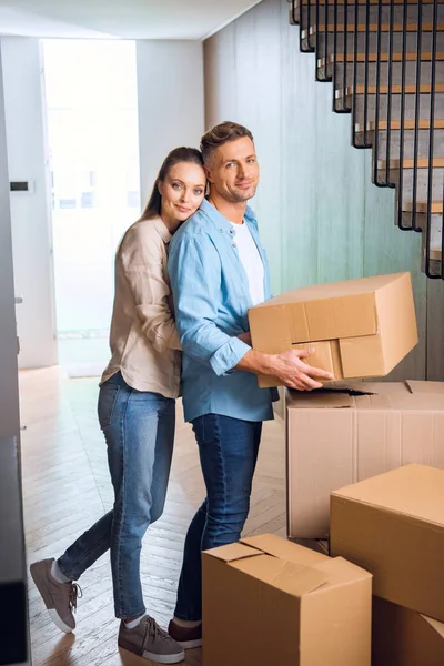 Felice donna che abbraccia bel marito con scatola in mano nella nuova casa — Foto stock