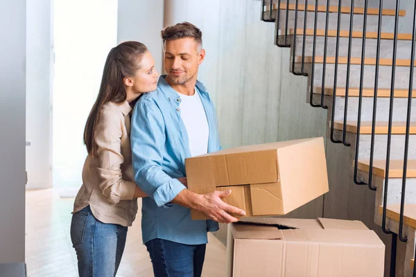 Attractive woman hugging handsome husband with box in hands in new home — Stock Photo