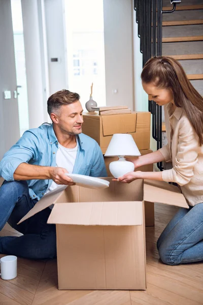 Alegre marido mirando la lámpara en manos de la esposa mientras está sentado en el suelo — Stock Photo