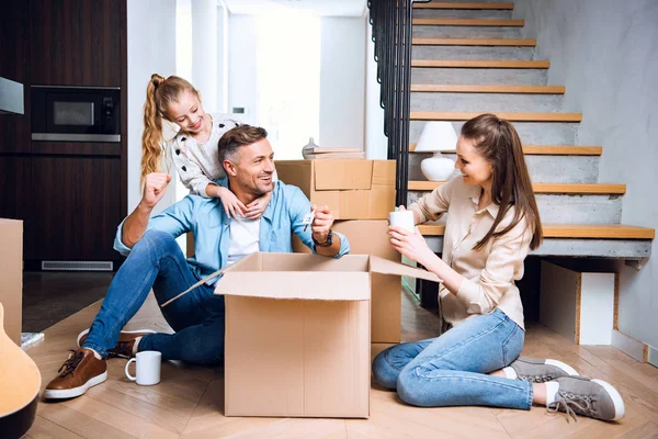 Cheerful child hugging father sitting on floor with cup of drink near wife — Stock Photo