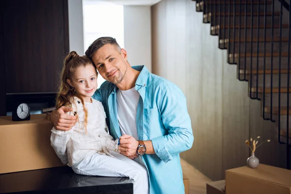 Feliz padre sosteniendo llavero y abrazando linda hija sentado en la mesa - foto de stock