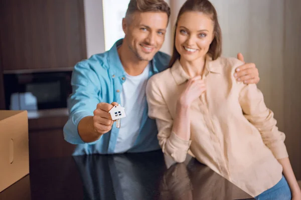 Selective focus of house shaped key chain in hand of handsome man hugging wife — Stock Photo