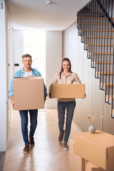 Couple heureux marchant avec des boîtes et souriant dans une nouvelle maison — Photo de stock