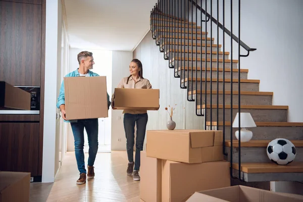 Счастливая пара, идущая с коробками и улыбающаяся в новом доме — стоковое фото