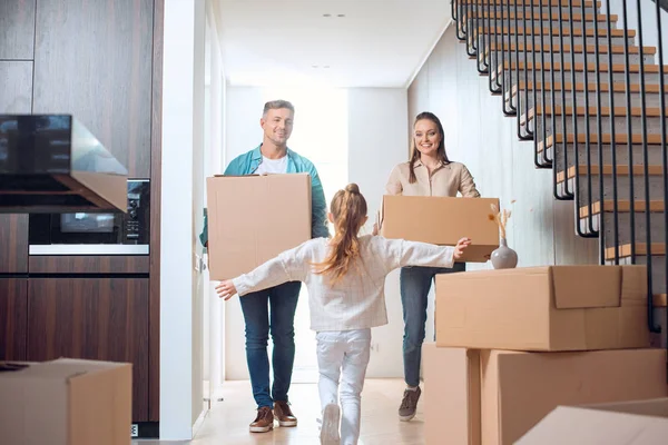Foco seletivo de criança correndo olhando para pais felizes segurando caixas em nova casa — Fotografia de Stock