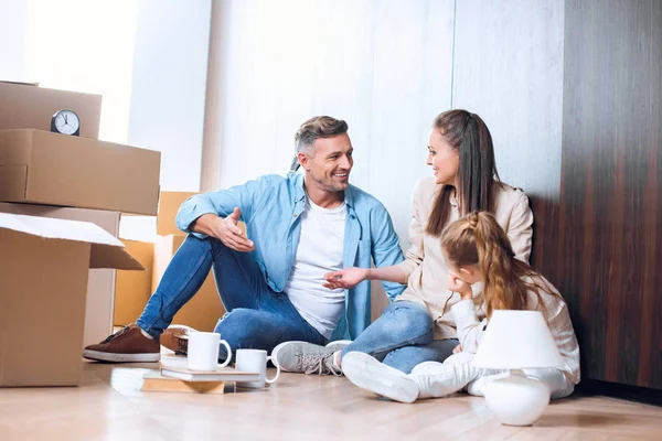 Feliz hombre sentado en el suelo y hablando con su esposa cerca de su hija - foto de stock