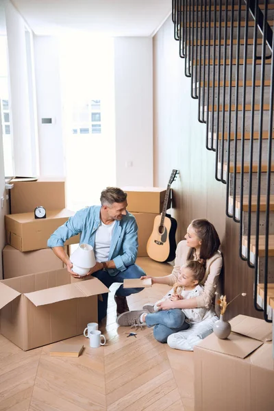 Щаслива сім'я сидить на підлозі біля коробок в новому будинку — стокове фото