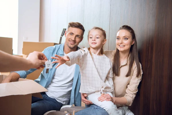 Selective focus of smiling kid taking house shaped key chain while sitting near parents — Stock Photo