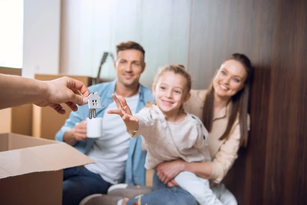 Selective focus of house shaped key chain with smiling kid sitting near parents on background — Stock Photo