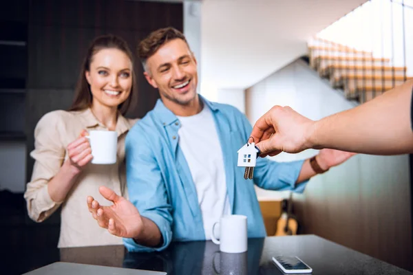 Selective focus of man giving house shaped key chain to happy couple in new home — Stock Photo