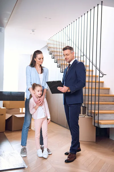 Handsome broker holding clipboard and standing near attractive woman with daughter — Stock Photo