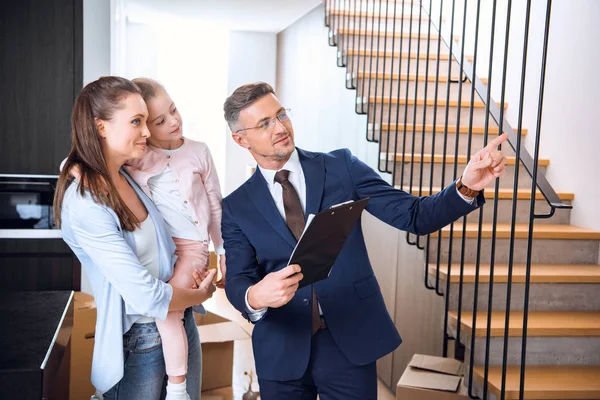 Schöner Makler zeigt Frau mit süßer Tochter etwas in den Armen — Stockfoto