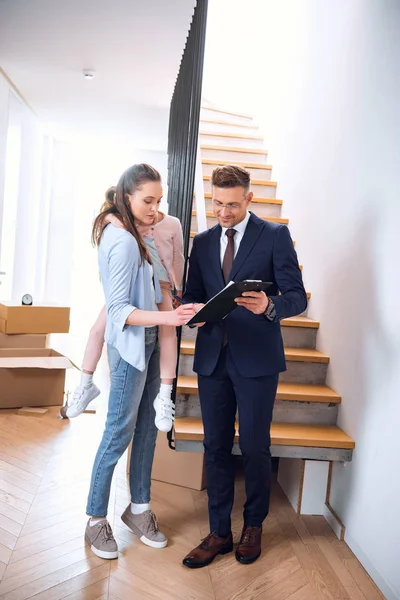 Mujer sosteniendo en brazos hija y firma documento cerca corredor celebración portapapeles — Stock Photo