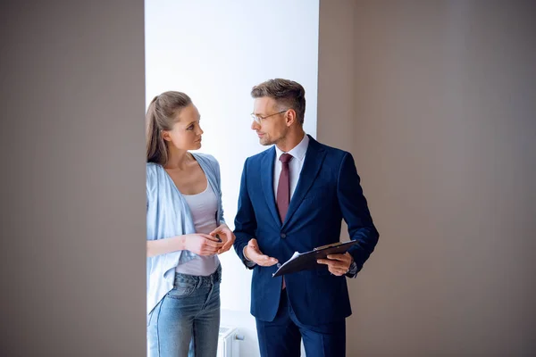 Schöner Makler, der schöne Frau ansieht, während er im Zimmer steht — Stockfoto